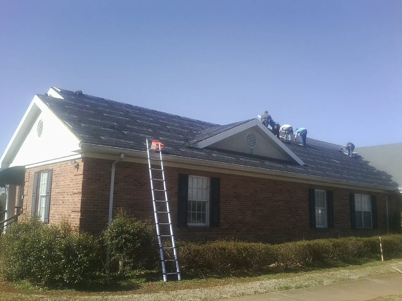Crew tearing shingles off a brick ranch roof with a ladder set — Emergency Roof Repair work by our crew in Powell
