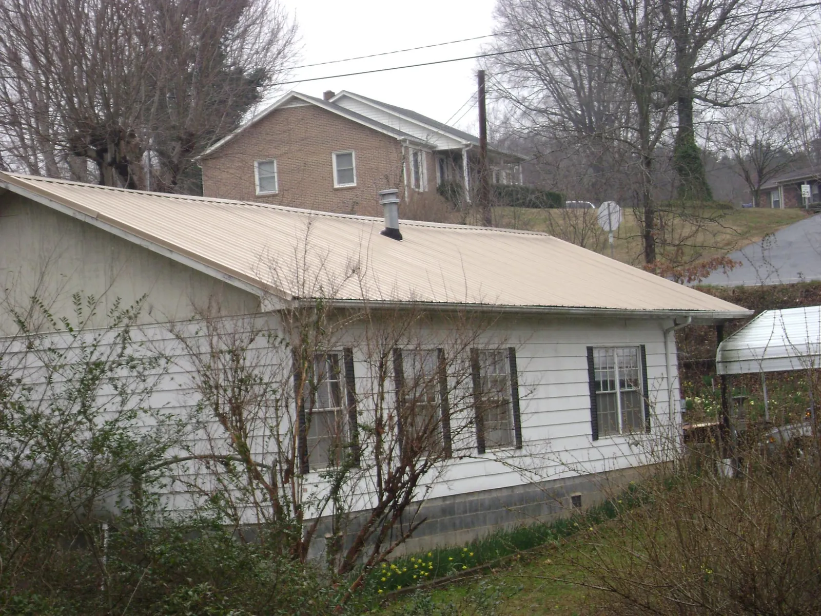 Tan metal roof on a white sided house set into a hillside — Commercial Roofing by Roofing Brothers in Powell